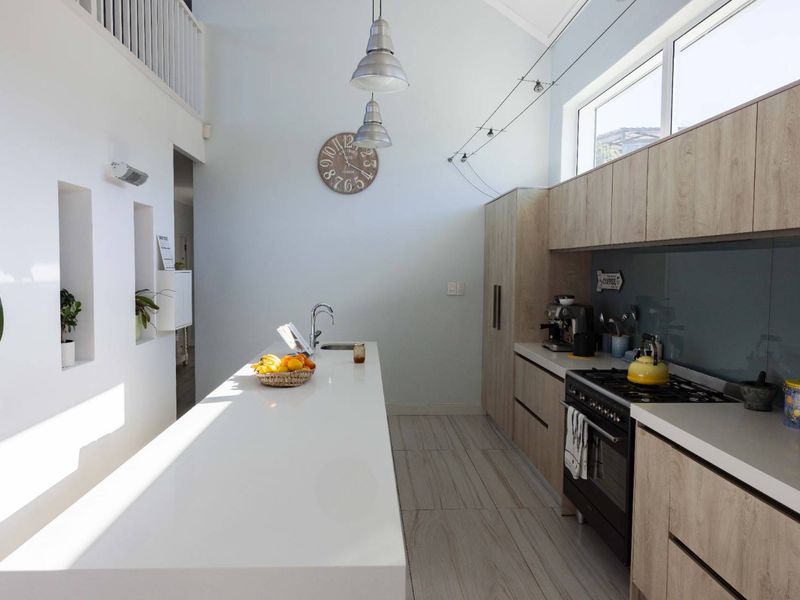 Modern kitchen featuring a long central island with stone countertops, light wood cabinetry, gas stove, and high ceilings with ample natural light.