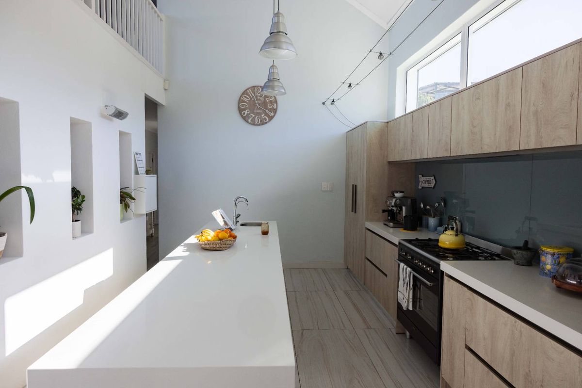 Modern kitchen featuring a long central island with stone countertops, light wood cabinetry, gas stove, and high ceilings with ample natural light.