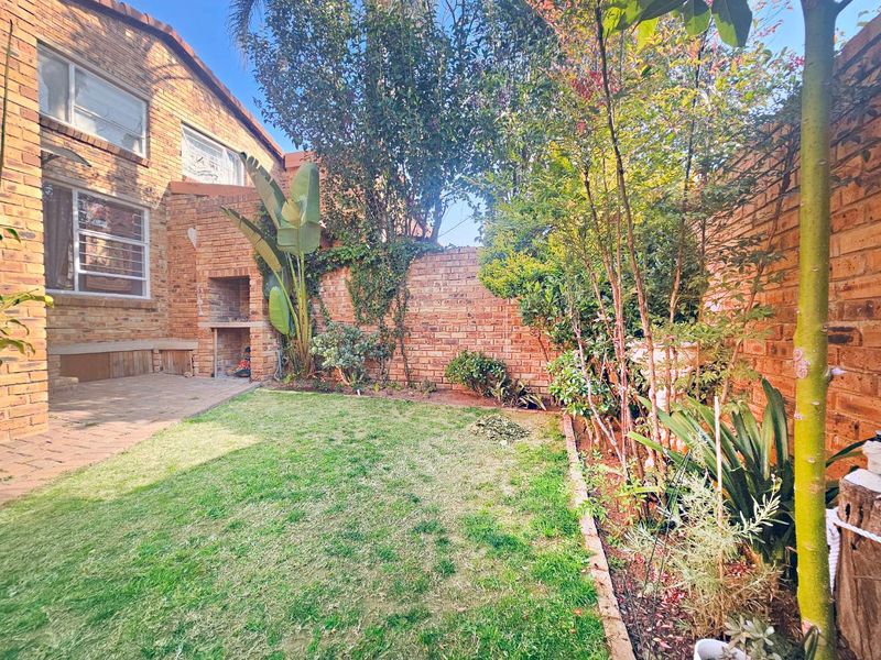 Private rear garden featuring a paved patio area with a built-in braai, established landscaping, and brick boundary walls.