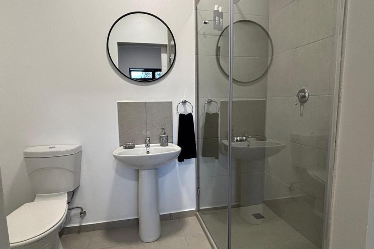 Modern bathroom featuring a glass-enclosed walk-in shower, pedestal basin, and toilet with neutral floor and wall tiling.
