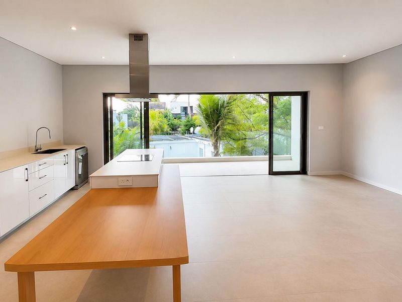 Modern open-plan kitchen and living area featuring sleek white cabinetry, integrated appliances, a central island, and large sliding doors opening to a balcony.