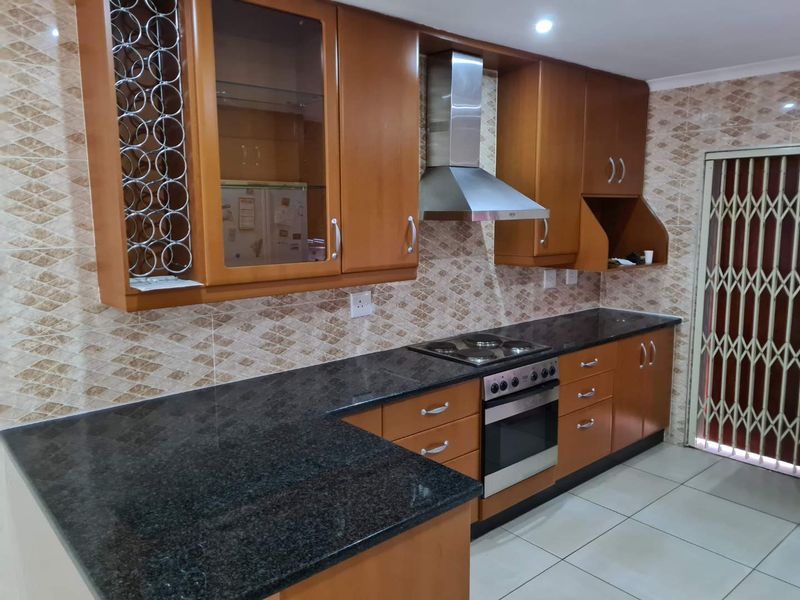 A functional kitchen featuring wooden cabinetry, granite countertops, a built-in oven with hob, stainless steel extractor fan, and decorative tiled backsplash.