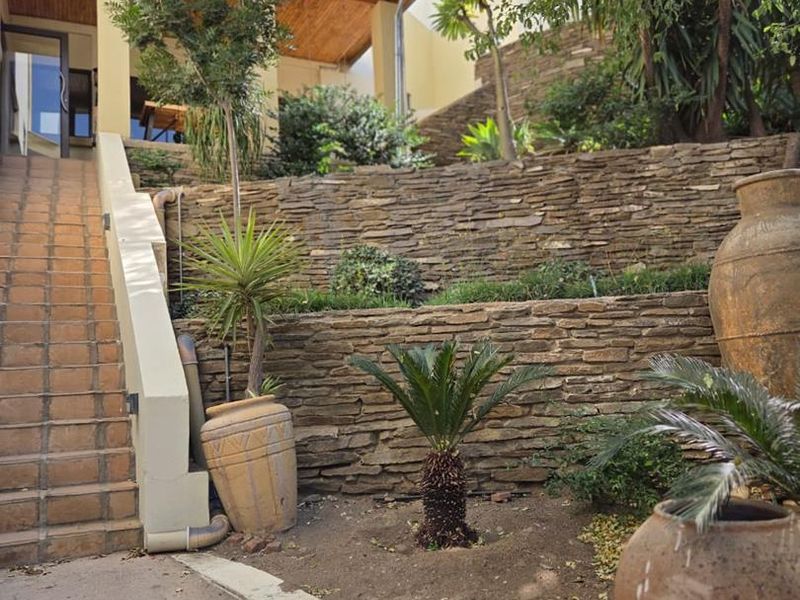 Rear exterior view featuring tiered stone retaining walls, a concrete staircase leading to a covered patio area with timber ceiling finishes.
