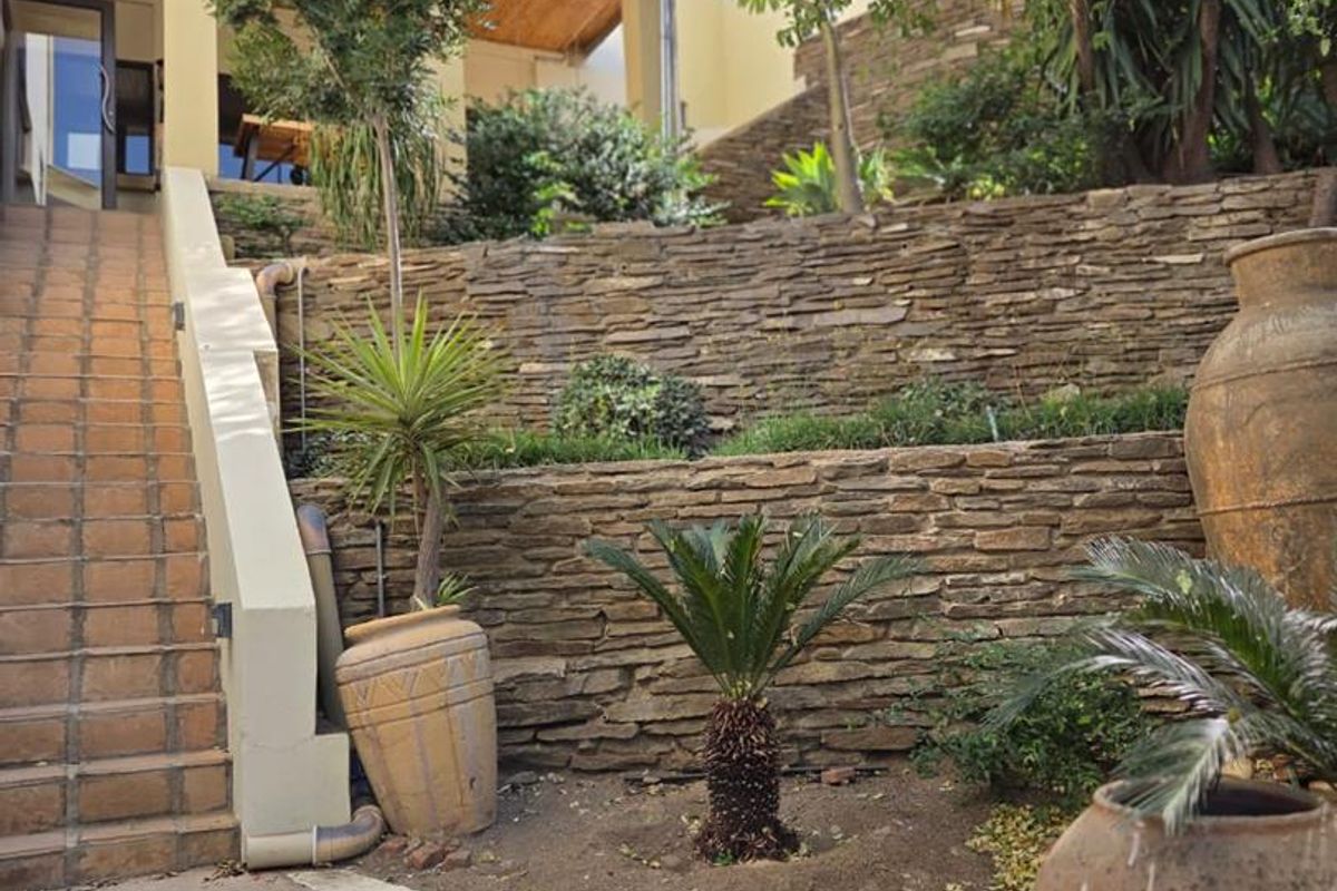 Rear exterior view featuring tiered stone retaining walls, a concrete staircase leading to a covered patio area with timber ceiling finishes.