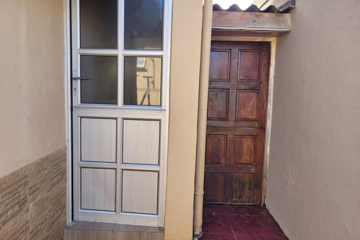 Rear exterior view showing a modern aluminium door alongside a traditional timber door with tiled flooring and external wall finishes.