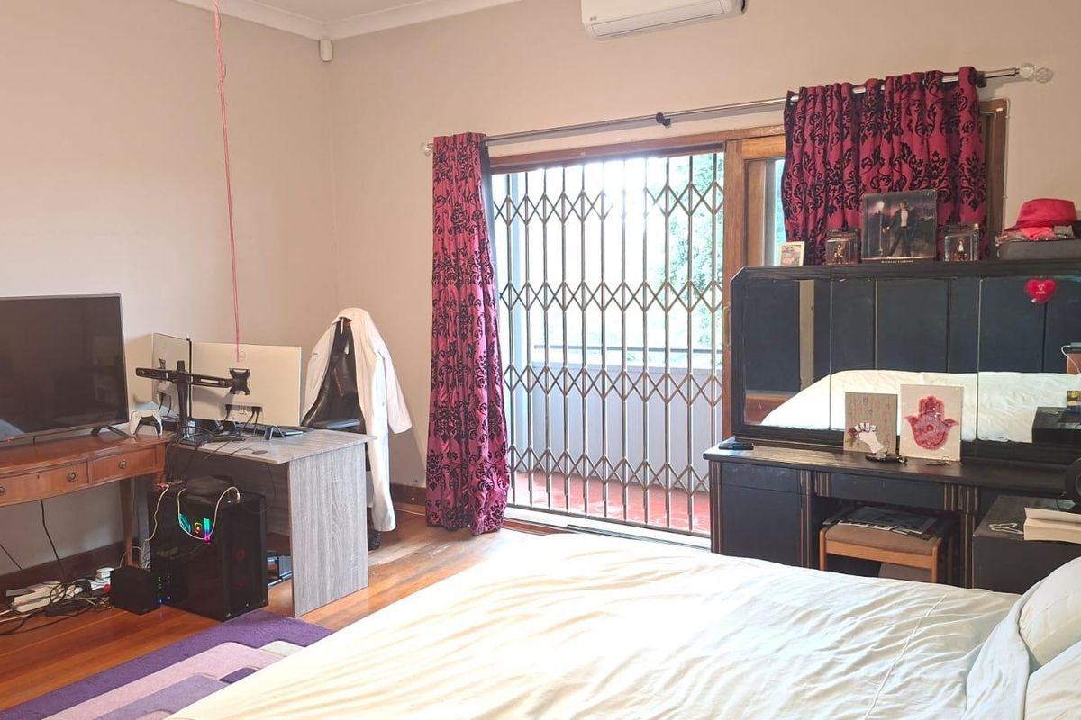 A bedroom featuring timber flooring, a wall-mounted air conditioning unit, and a sliding glass door with a security gate leading to an outdoor area.