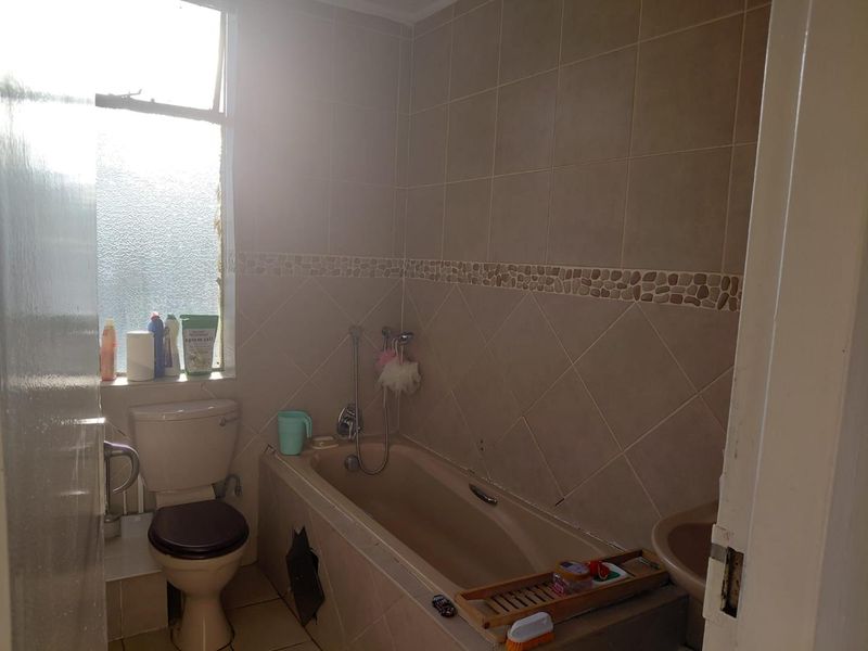 A functional bathroom featuring a bathtub with shower mixer, toilet, and tiled finishes. The space requires minor repairs to the bathtub panel.