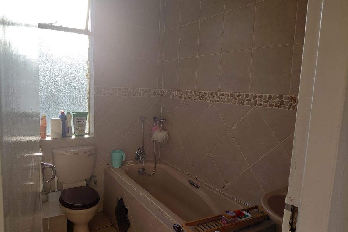A functional bathroom featuring a bathtub with shower mixer, toilet, and tiled finishes. The space requires minor repairs to the bathtub panel.
