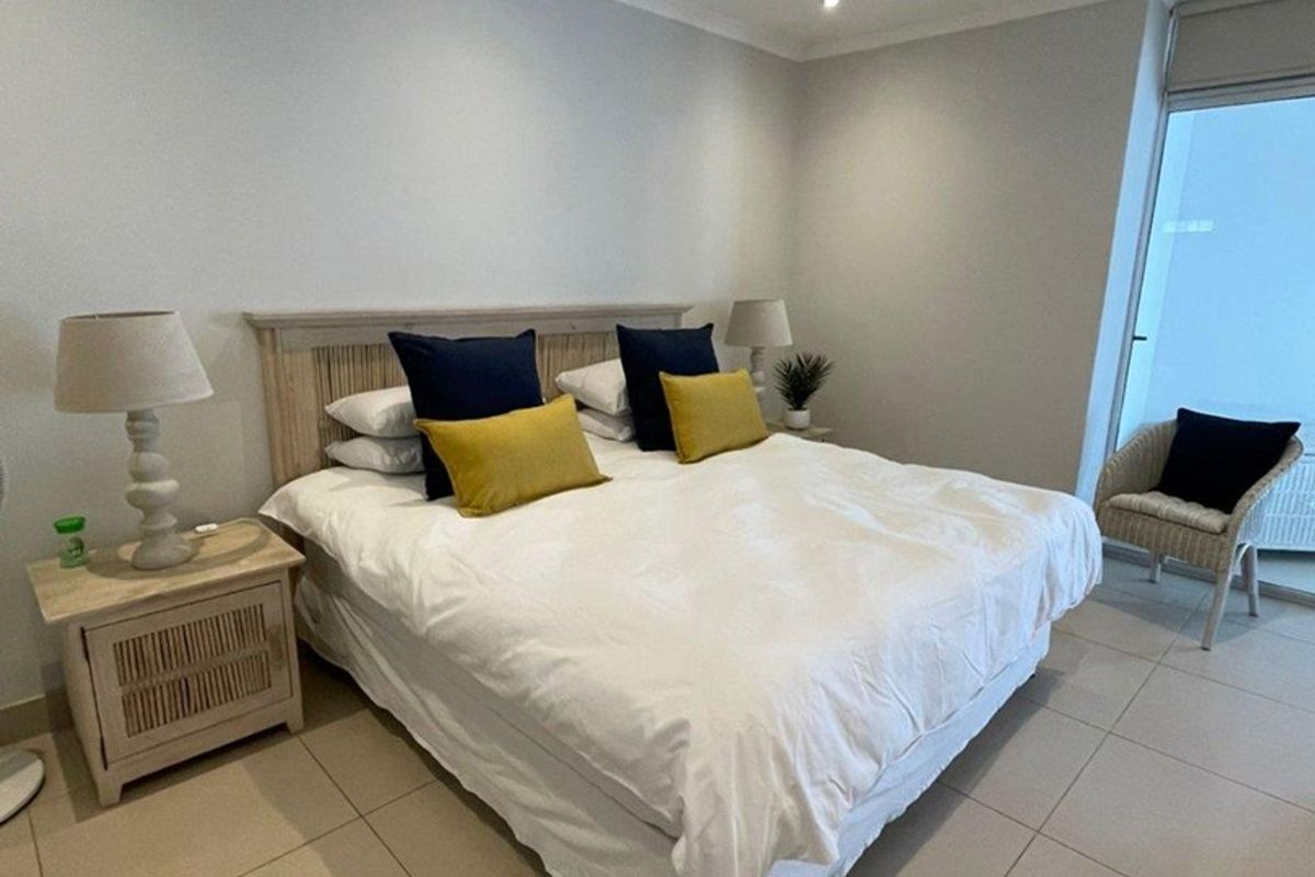 A well-maintained bedroom featuring neutral tiled flooring, recessed downlighting, and direct access to an outdoor area through a sliding glass door.