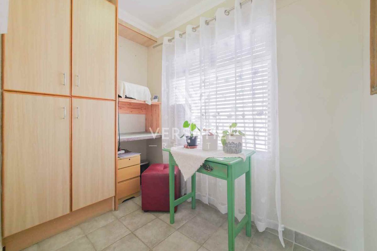 A compact bedroom featuring built-in wooden cupboards and tiled flooring, offering a functional space with natural light from the window.