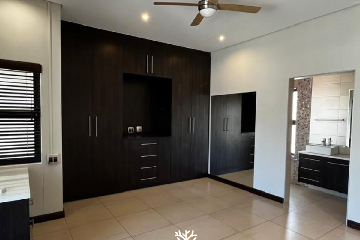 Spacious bedroom featuring extensive dark wood built-in cabinetry, tiled flooring, a ceiling fan, and an adjoining en-suite bathroom with a modern vanity.