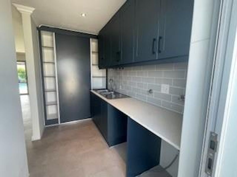 A modern, well-appointed scullery featuring dark cabinetry, stone countertops, a subway tile backsplash, and integrated sink, offering ample storage and prep space.