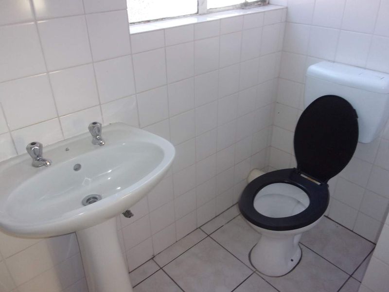 A compact bathroom featuring a white pedestal basin and a standard toilet with tiled walls and flooring throughout.