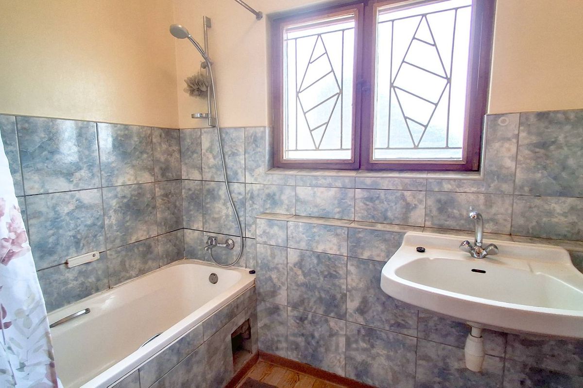 A functional bathroom featuring a bathtub with shower mixer, wall-mounted basin, and tiled walls. The space requires minor repairs and cosmetic updates.