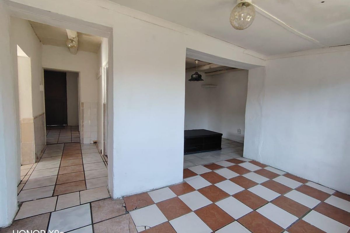 An empty living area featuring checkered ceramic floor tiles and basic ceiling lighting, showing signs of wear and requiring cosmetic updates.