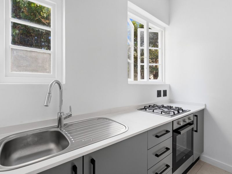 A modern, clean kitchen featuring grey cabinetry, stone countertops, a stainless steel sink, and built-in gas hob and oven.