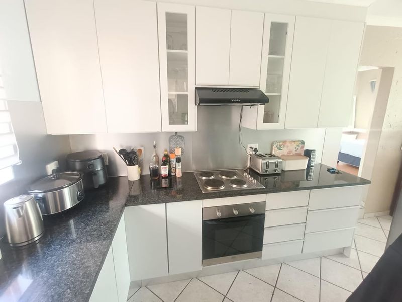 A functional kitchen featuring white cabinetry, granite countertops, a stainless steel splashback, and integrated electric cooking appliances with tiled flooring.