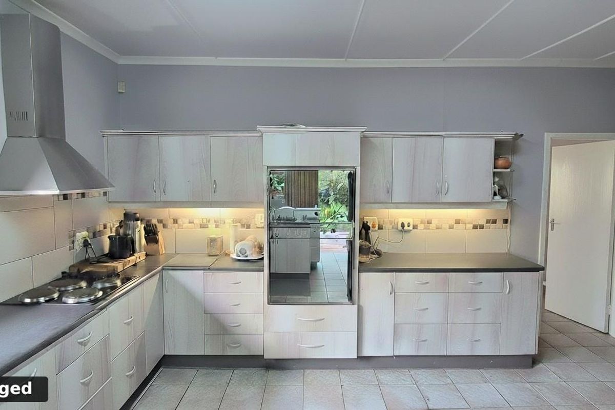 A functional kitchen featuring light wood-grain cabinetry, dark countertops, a stainless steel extractor fan, and tiled flooring with a neutral backsplash.