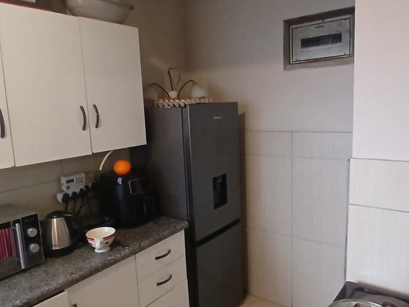 A compact kitchen featuring white cabinetry, stone countertops, and tiled splashbacks, with an integrated electrical distribution board visible on the wall.