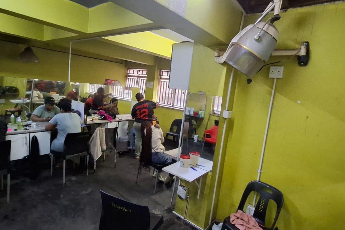 A commercial salon space featuring wall-mounted hair dryers, large mirrors, and exposed ceiling beams, currently set up as a functional hair styling area.
