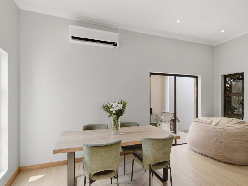 A bright and modern living area featuring neutral walls, timber-look flooring, recessed lighting, and a wall-mounted split-system air conditioner with access to the outdoors.