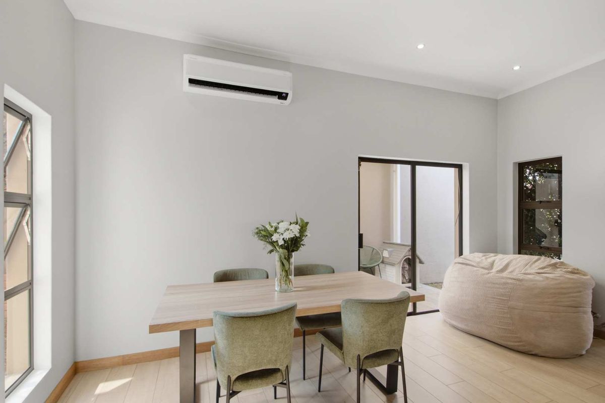A bright and modern living area featuring neutral walls, timber-look flooring, recessed lighting, and a wall-mounted split-system air conditioner with access to the outdoors.