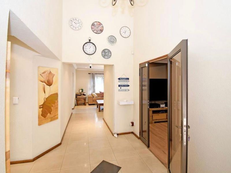 Spacious entrance hall featuring high ceilings, neutral tiled flooring, and direct access to the adjoining living area through glass-panelled doors.