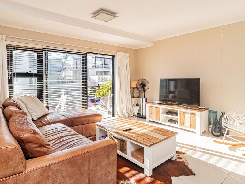 A bright living room featuring large sliding glass doors with venetian blinds, neutral walls, and polished tiled flooring.