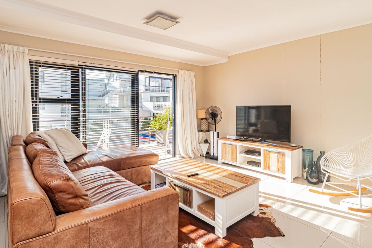 A bright living room featuring large sliding glass doors with venetian blinds, neutral walls, and polished tiled flooring.