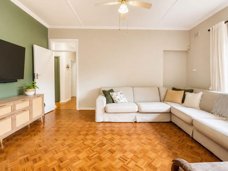 A well-maintained living room featuring classic parquet flooring, a ceiling fan, and a neutral color palette with a green accent wall.