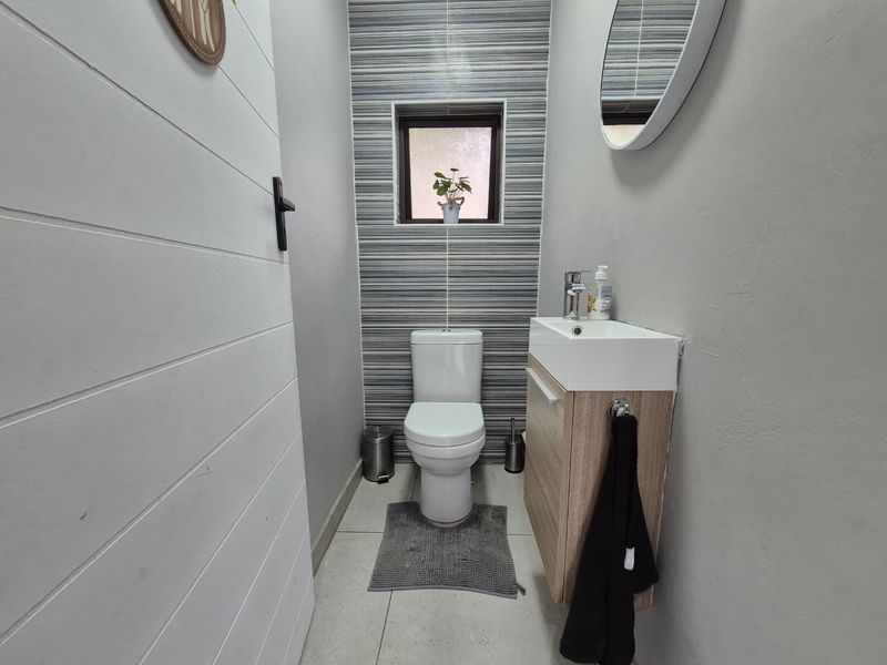 A compact, modern guest bathroom featuring a wall-mounted vanity, contemporary basin, and stylish horizontal-striped feature wall tiling.
