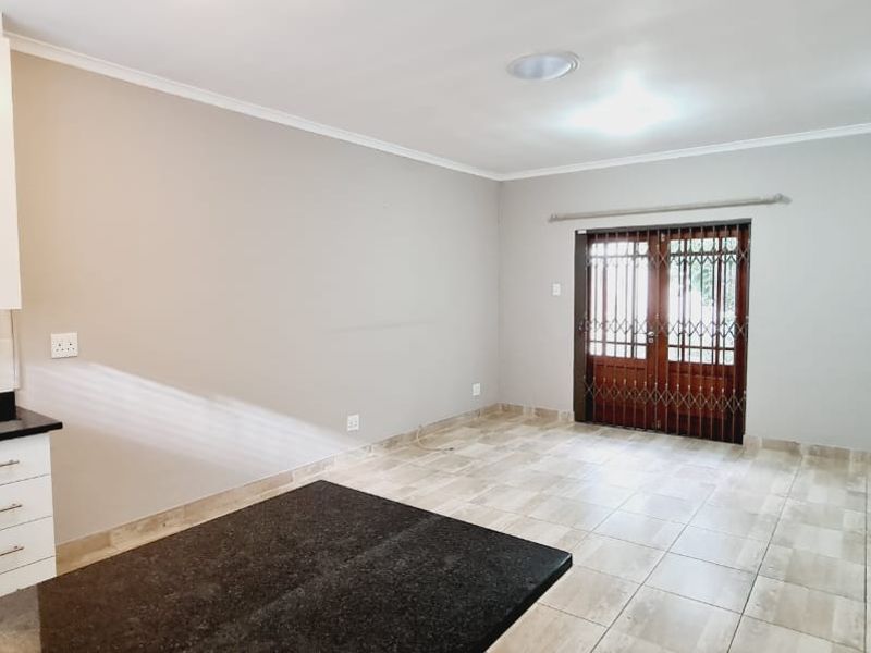 Open-plan living area featuring a modern kitchen with stone countertops and tiled flooring, leading out through a security gate to the exterior.