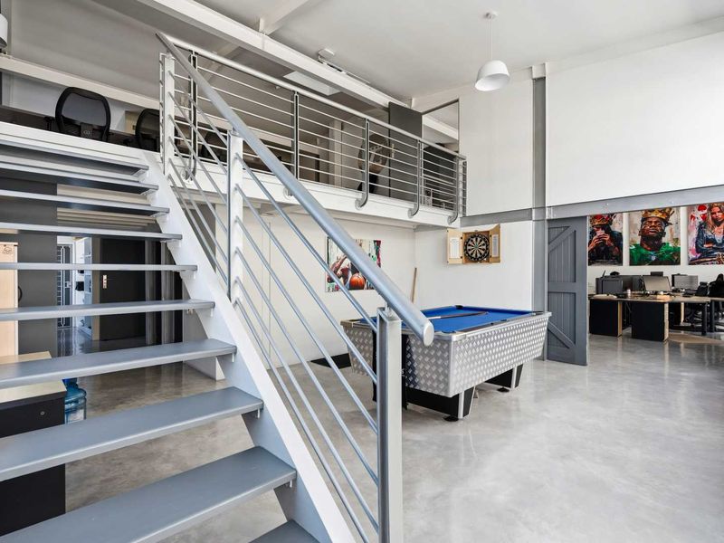Modern open-plan office space featuring a mezzanine level, polished concrete floors, and industrial-style exposed steel beams with a staircase.