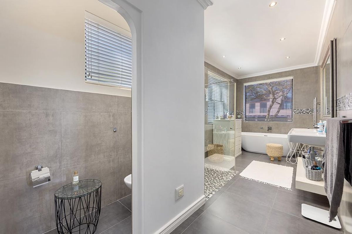 Modern bathroom featuring a freestanding bathtub, glass-enclosed shower, wall-mounted vanity, and contemporary grey tiling with mosaic accents.