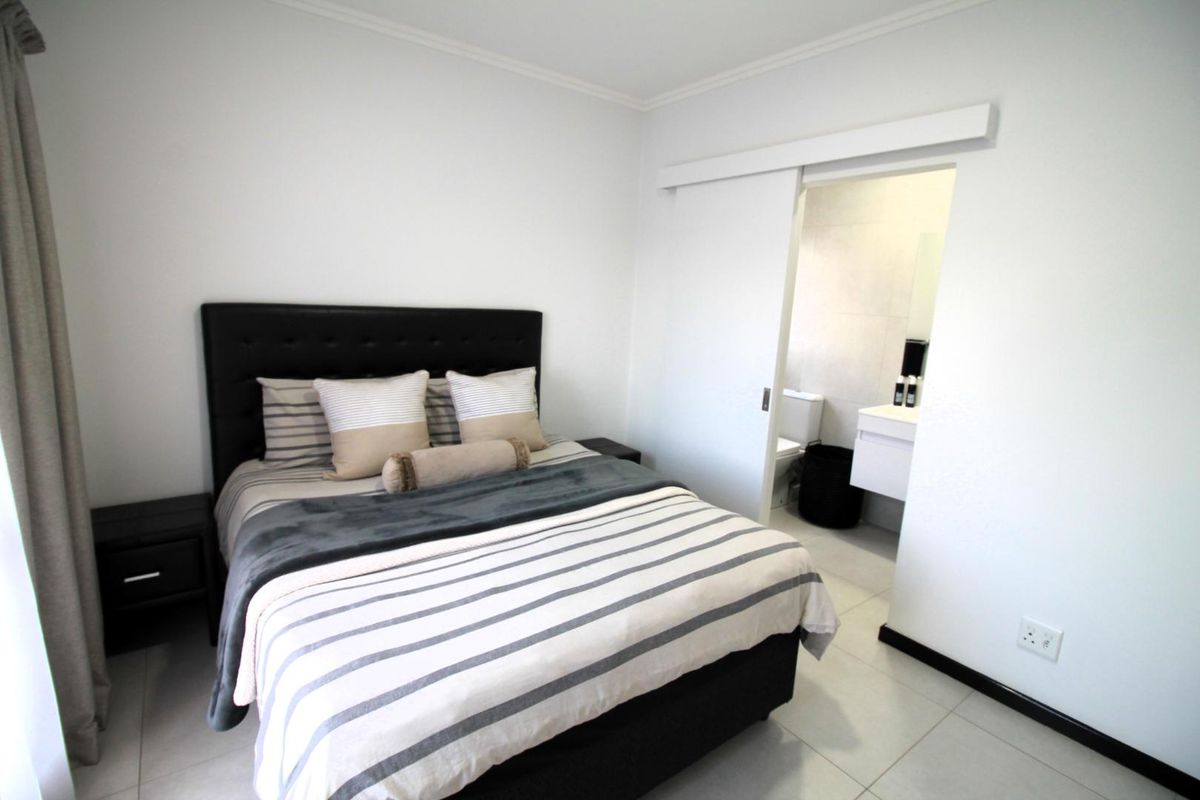A well-maintained bedroom featuring neutral tiled flooring and a sliding door providing direct access to an en-suite bathroom.