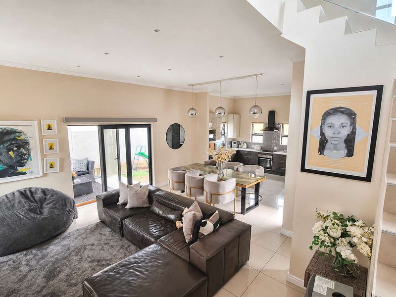 Spacious open-plan living and dining area featuring tiled floors, recessed lighting, a modern staircase with glass balustrade, and a well-appointed kitchen.