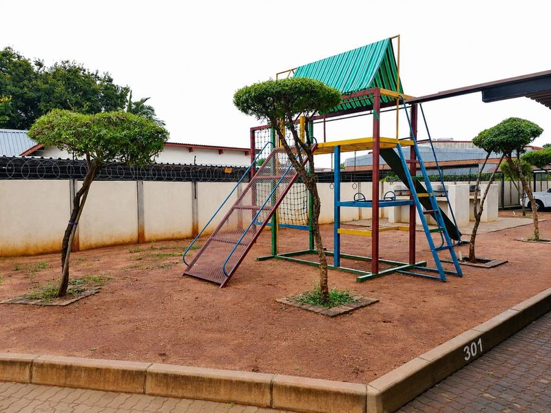Communal outdoor area featuring a playground structure, perimeter wall with security fencing, and paved curbing.