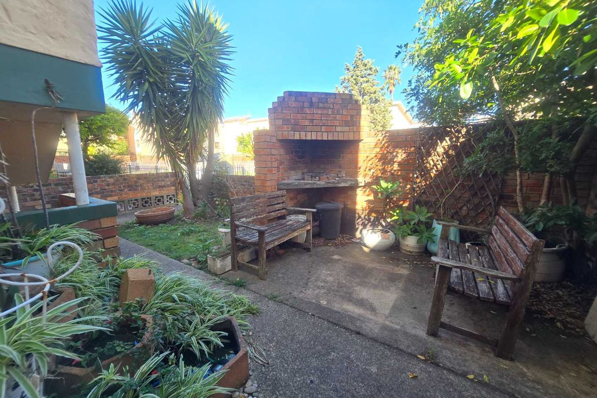A private rear courtyard featuring a built-in brick braai or barbecue area, concrete paving, and established garden landscaping.