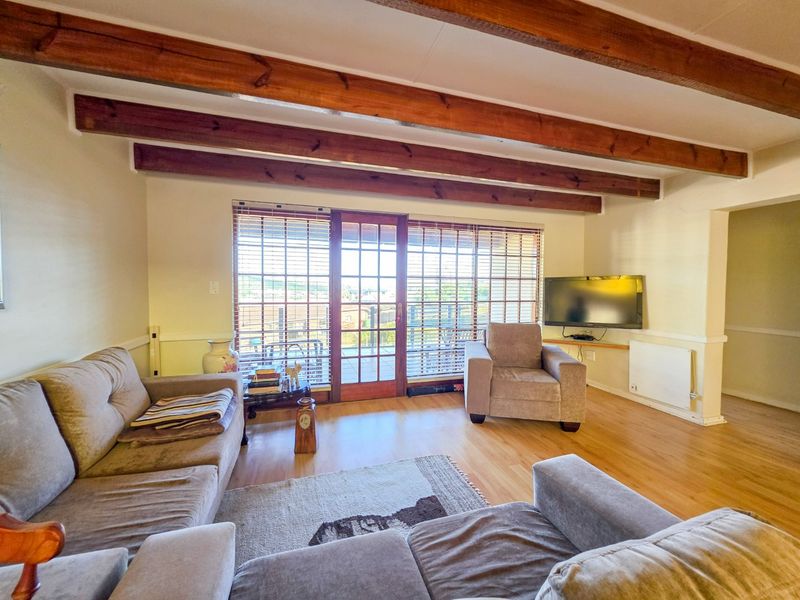 Spacious living room featuring exposed timber ceiling beams, laminate flooring, and a timber-framed glass door providing access to the outdoor area.
