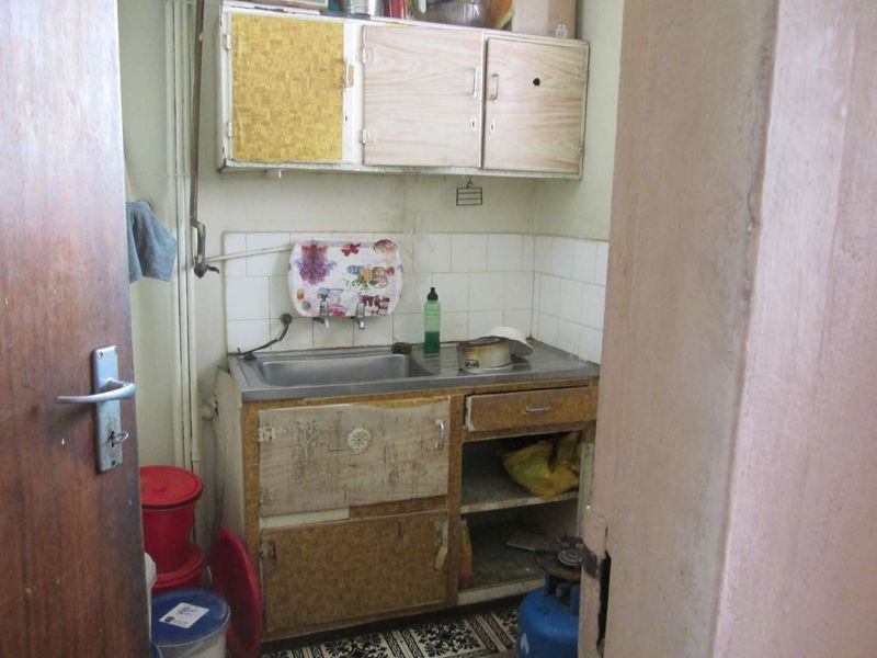 A compact, dated kitchen area featuring a stainless steel sink, tiled splashback, and original cabinetry in need of renovation.
