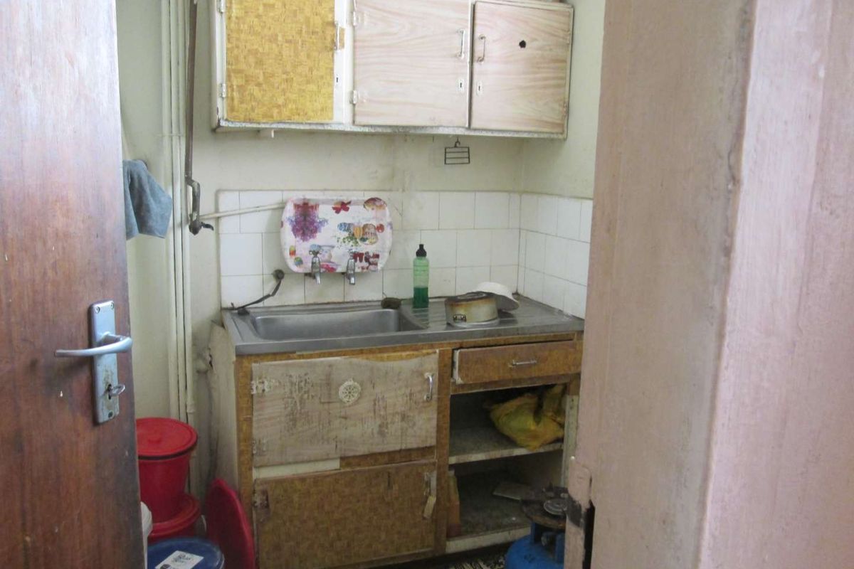 A compact, dated kitchen area featuring a stainless steel sink, tiled splashback, and original cabinetry in need of renovation.