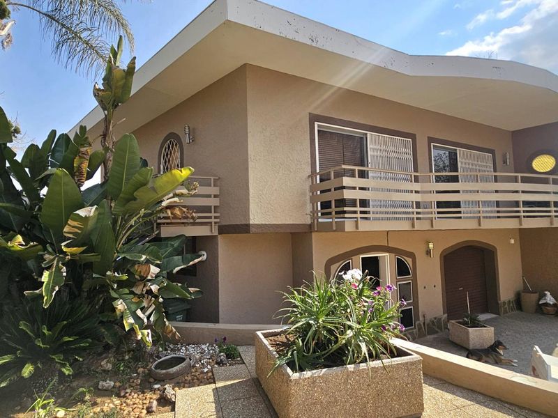 Two-story residential property featuring a balcony with security gates, paved driveway, and established garden beds.