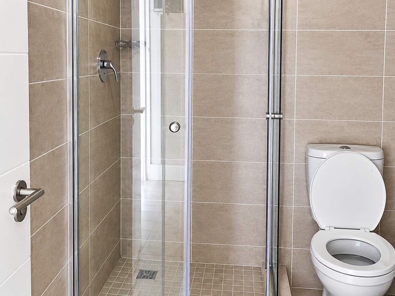 A clean, modern bathroom featuring a glass-enclosed shower, neutral ceramic wall tiling, and a standard toilet.