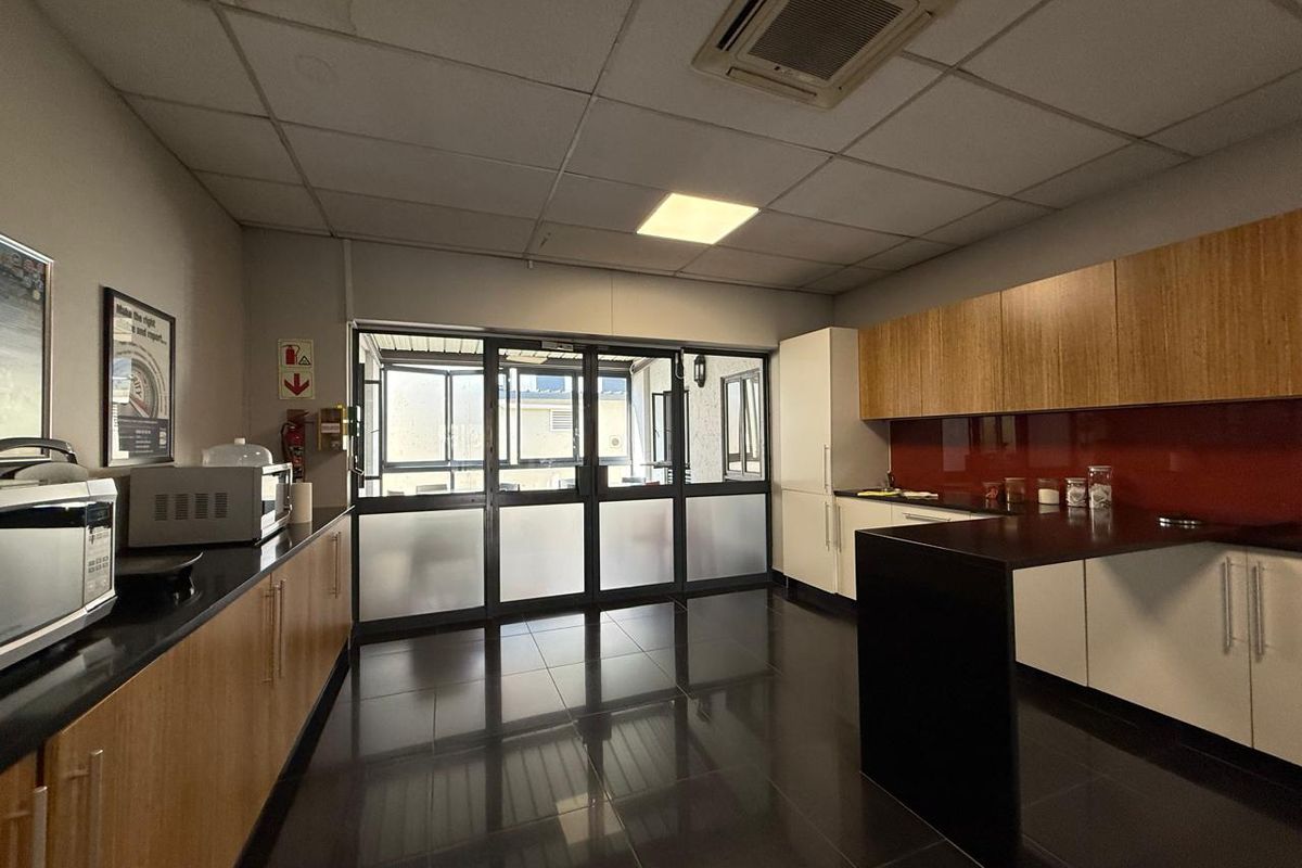 A functional office kitchenette featuring modern cabinetry, dark countertops, a glass splashback, and integrated ceiling air conditioning.