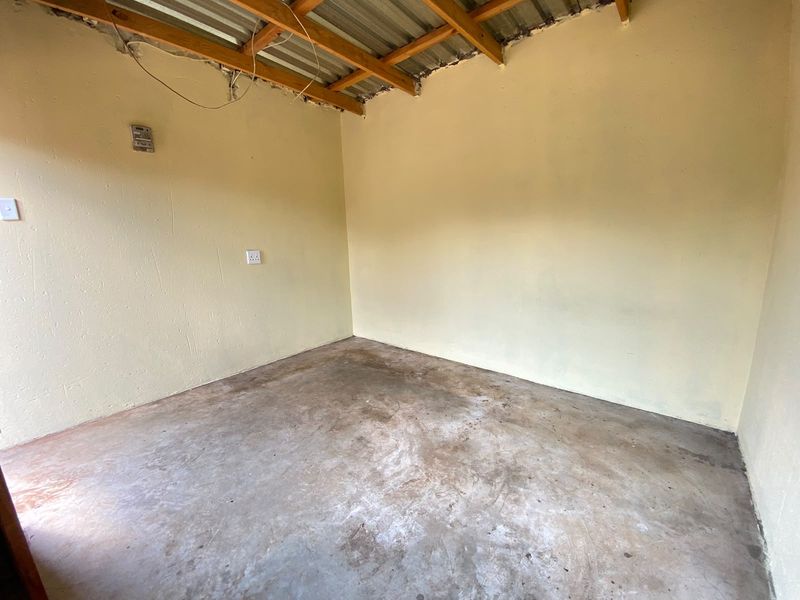 An unfinished utility space featuring exposed timber rafters, corrugated metal roofing, and a concrete floor, suitable for storage or workshop conversion.