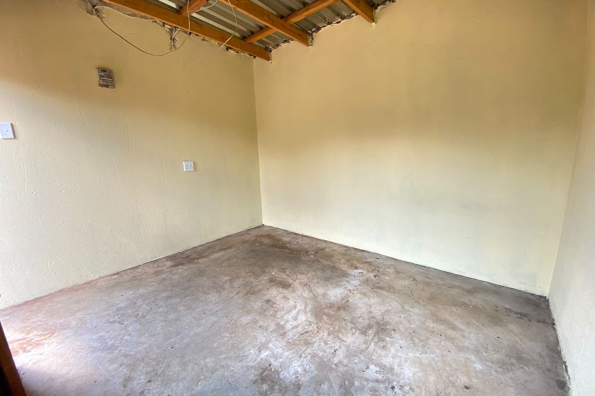 An unfinished utility space featuring exposed timber rafters, corrugated metal roofing, and a concrete floor, suitable for storage or workshop conversion.