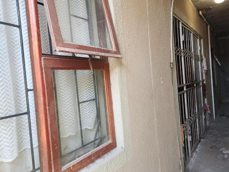 A narrow hallway or exterior passage featuring timber-framed windows, security gates, and exposed ceiling infrastructure, currently in need of significant maintenance and finishing.