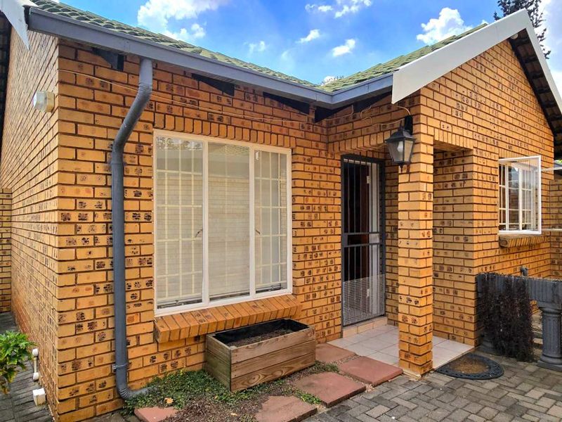 A well-maintained face brick townhouse exterior featuring a tiled roof, paved entrance area, and secure gated access.