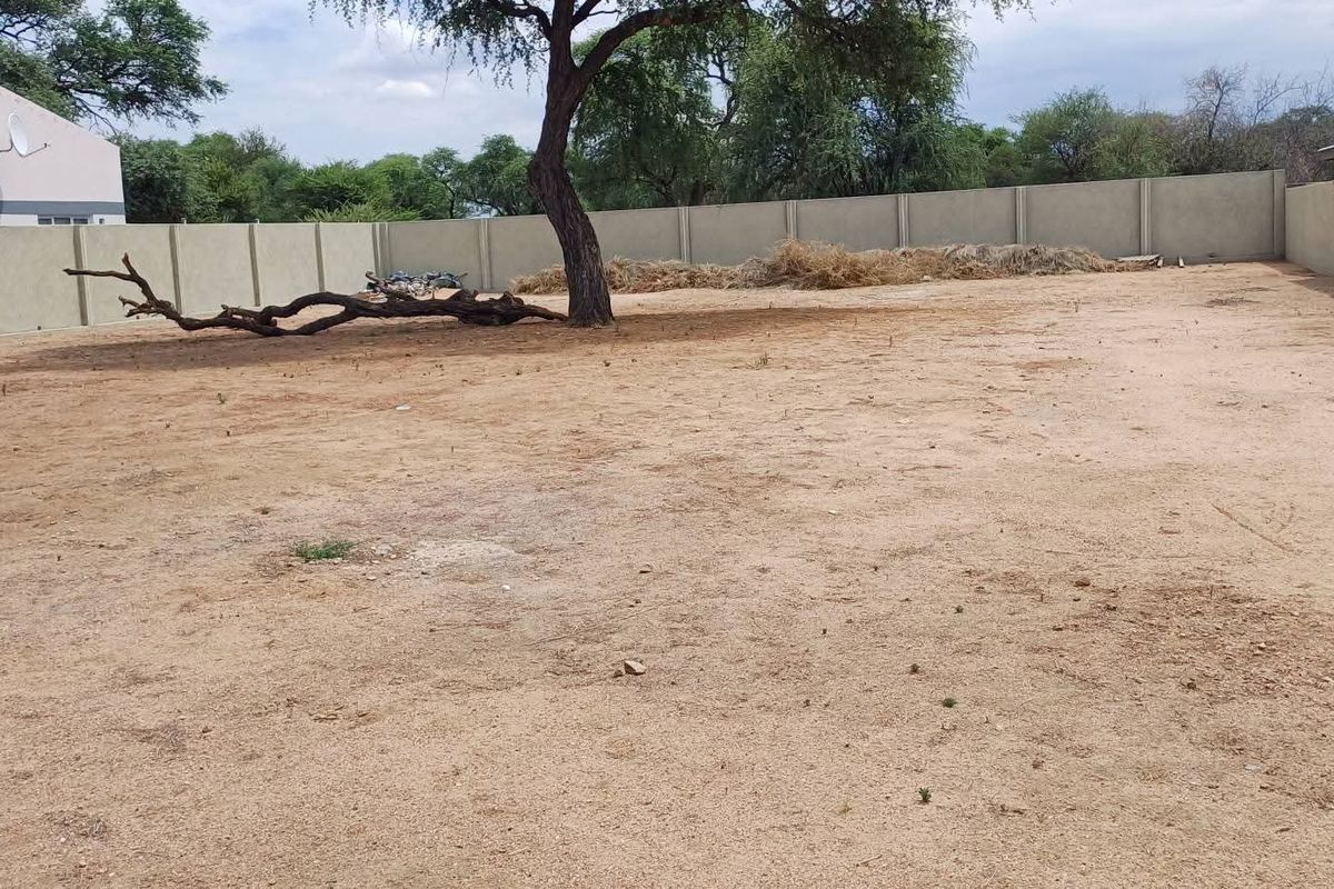 A vacant residential plot featuring a level sandy surface, a mature tree, and secure precast concrete boundary walls.