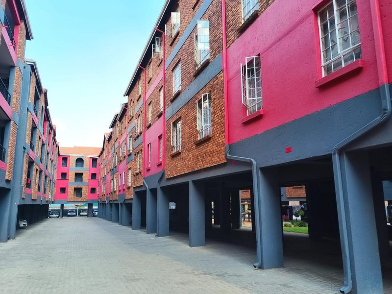 Exterior view of a multi-story apartment complex featuring brick and painted facade finishes with a paved ground-level parking area.